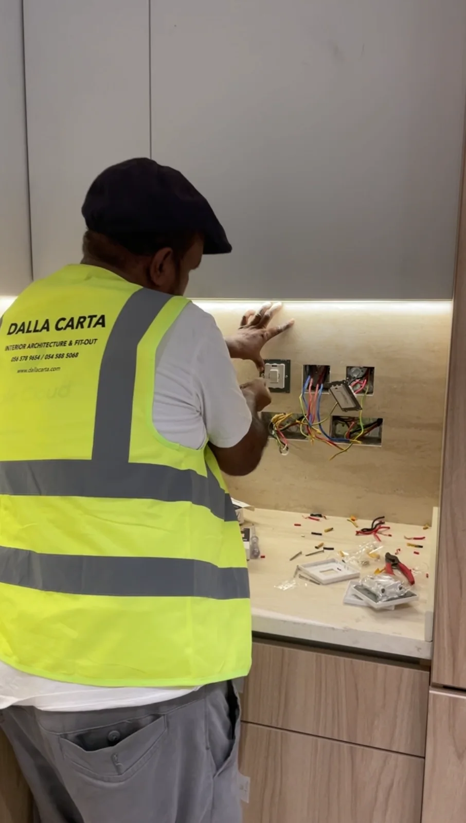 Dalla Carta team member installing kitchen electrical fittings beneath cabinet lighting